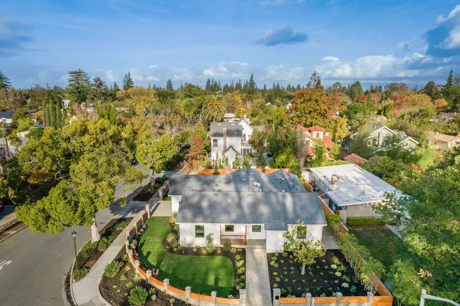 Aerial drone view of a suburban neighborhood with tree-lined streets and a renovated home with a new lawn and landscaping.