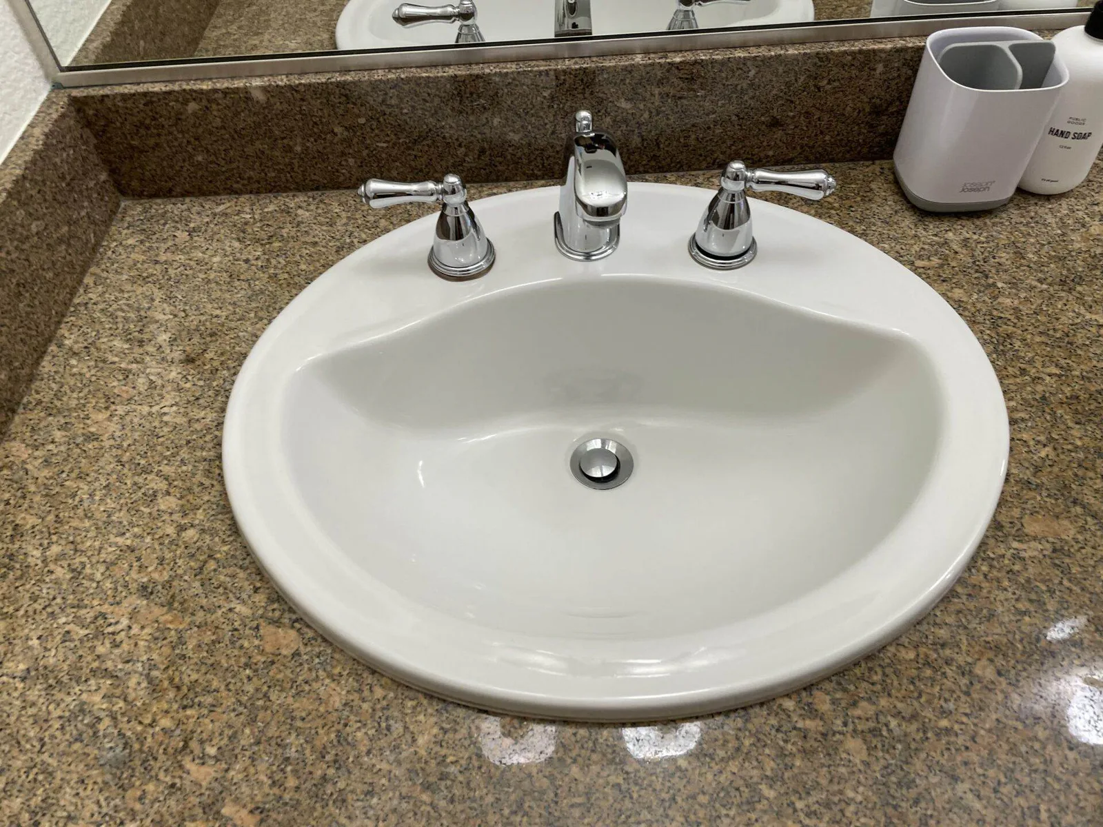 Clean oval porcelain bathroom sink with chrome faucet and handles on a granite countertop.