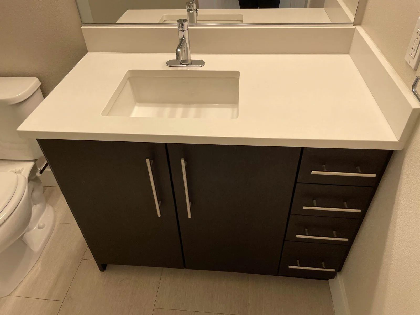Clean white quartz bathroom vanity countertop with an undermount sink and dark wood cabinet drawers below.