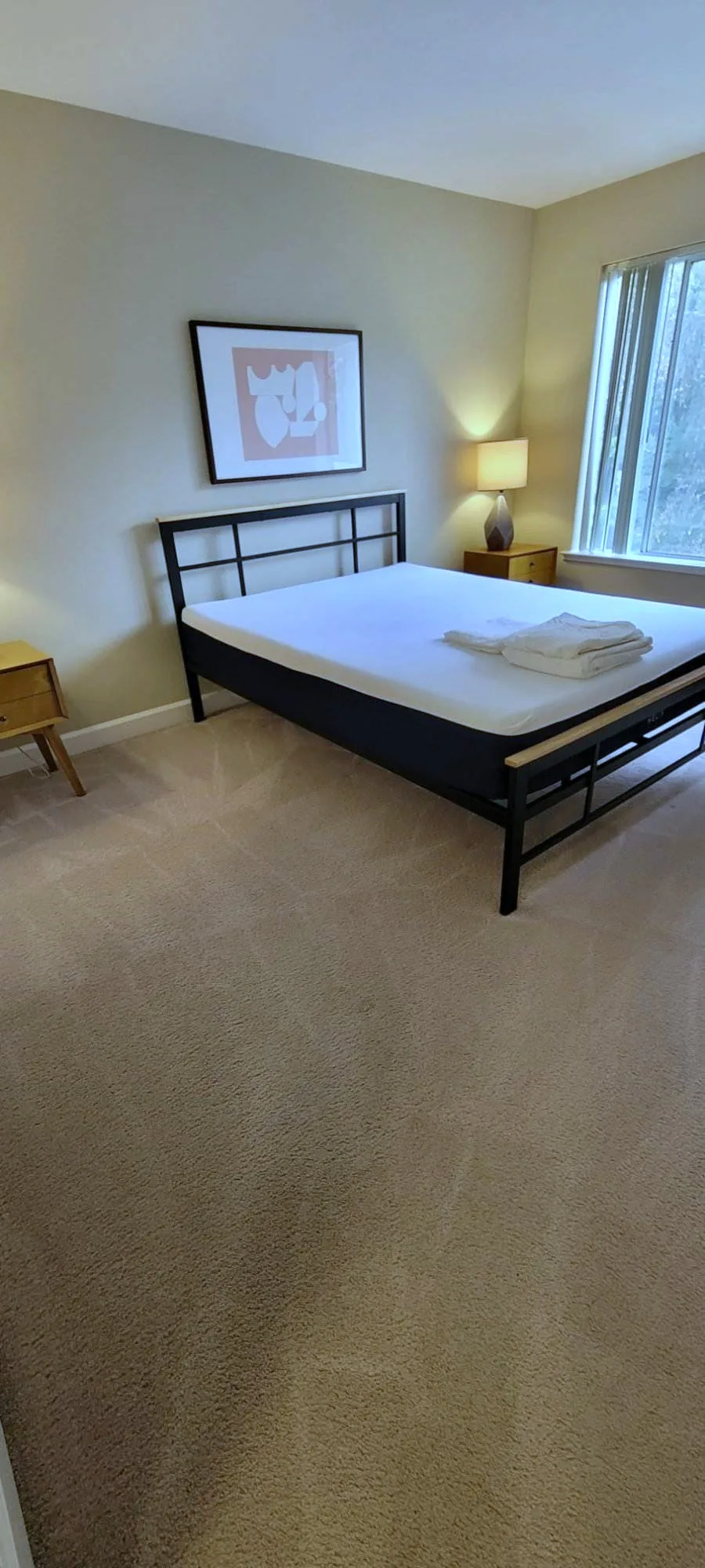 Bedroom with a bare mattress, folded white towels, and freshly cleaned beige carpet.