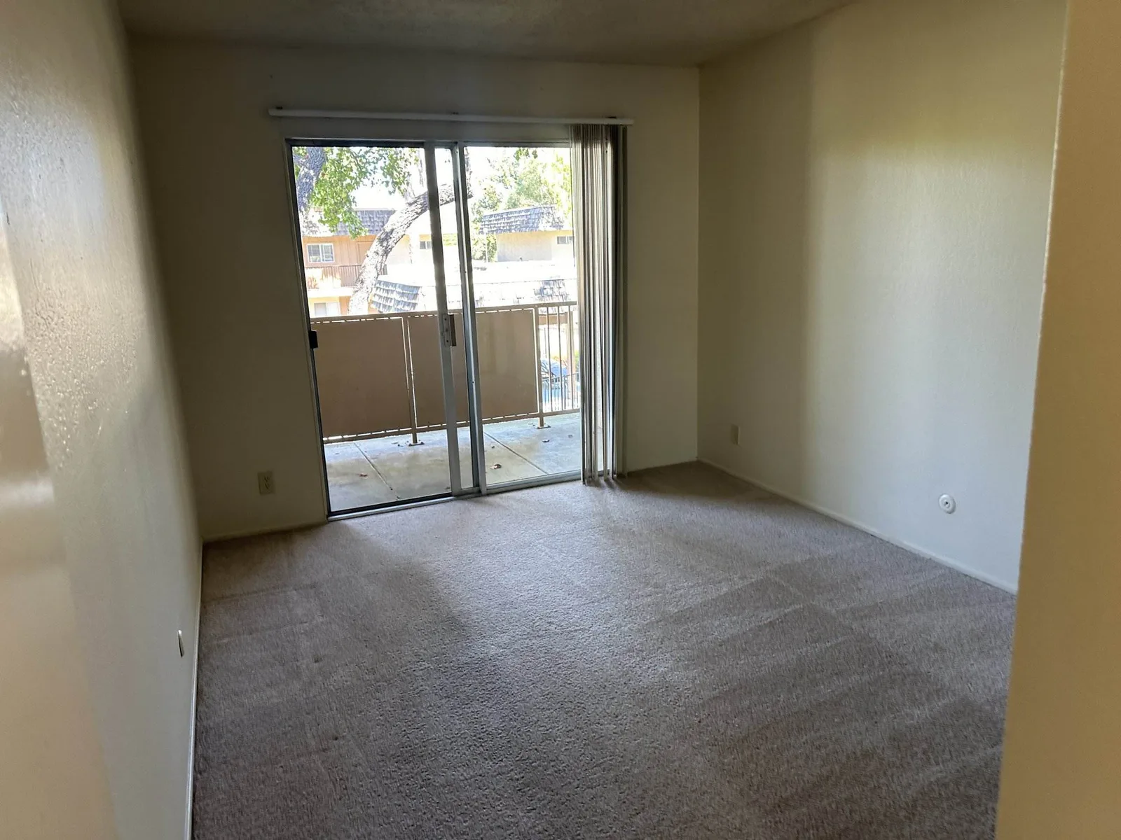 Empty carpeted bedroom with visible carpet-cleaning pass lines, a sliding glass door leading to a balcony.