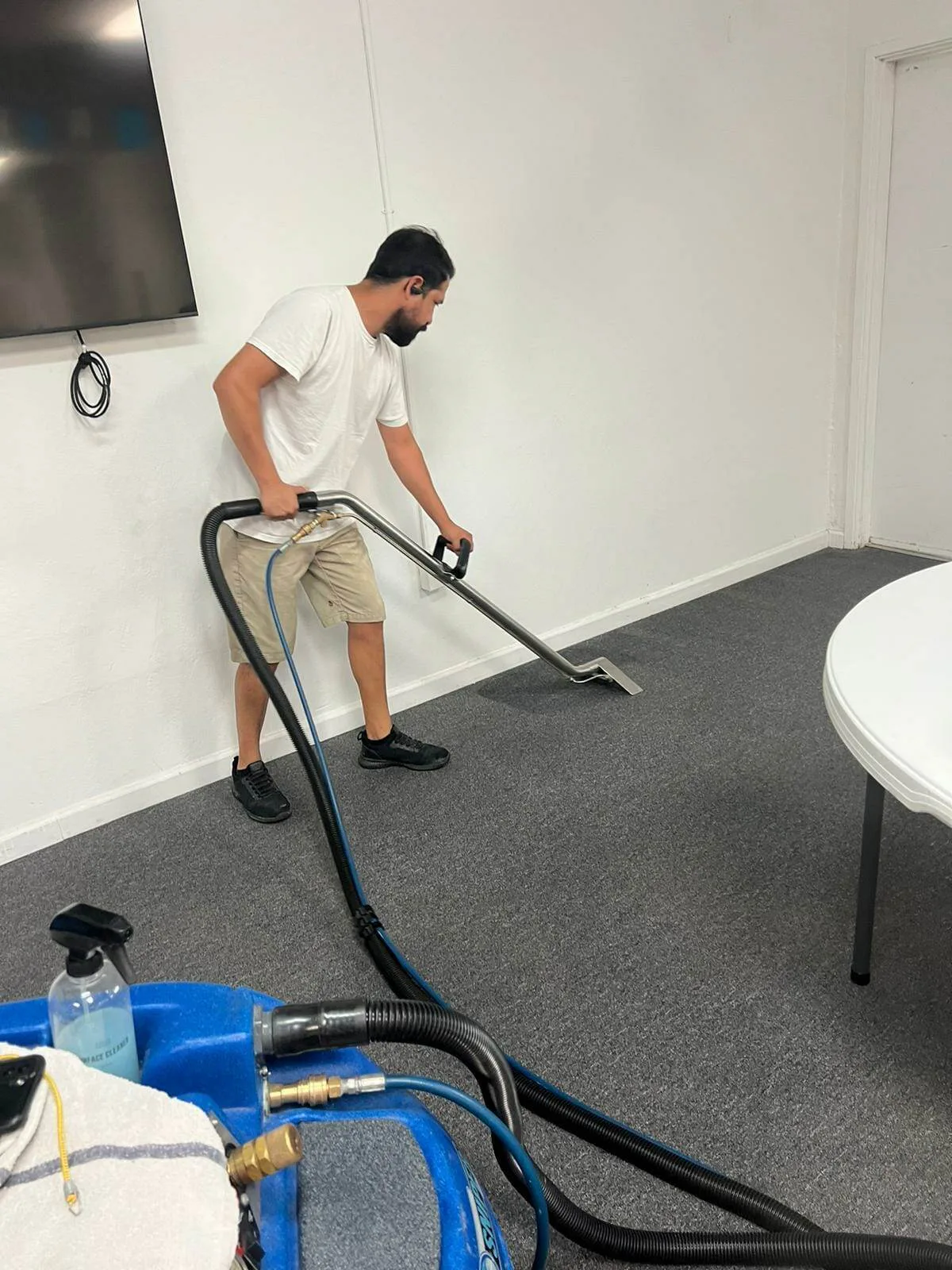Technician steam cleaning gray office carpet using a hose-connected extraction machine.