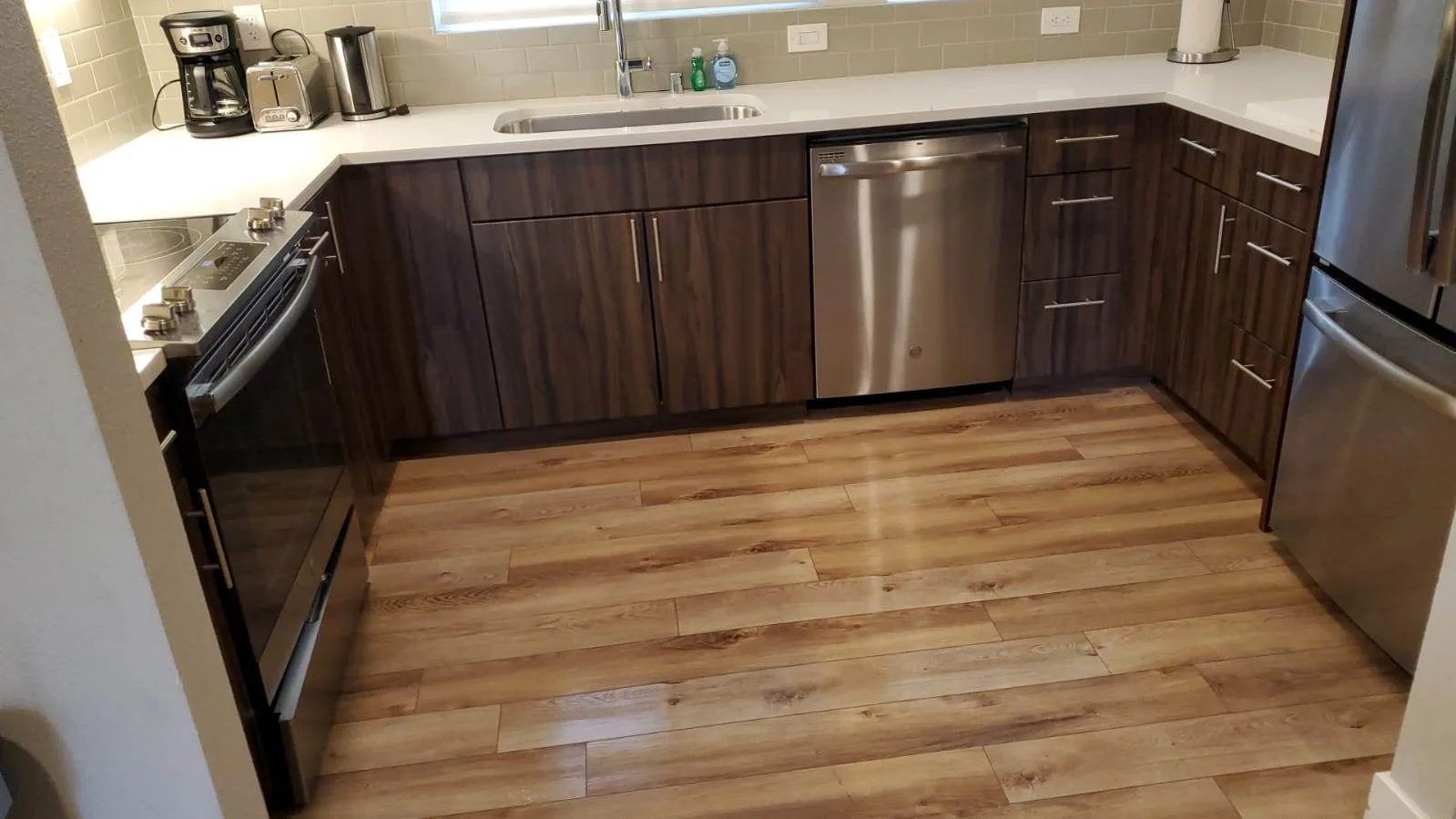 Kitchen with dark wood cabinets, stainless dishwasher and refrigerator, and light wood flooring.