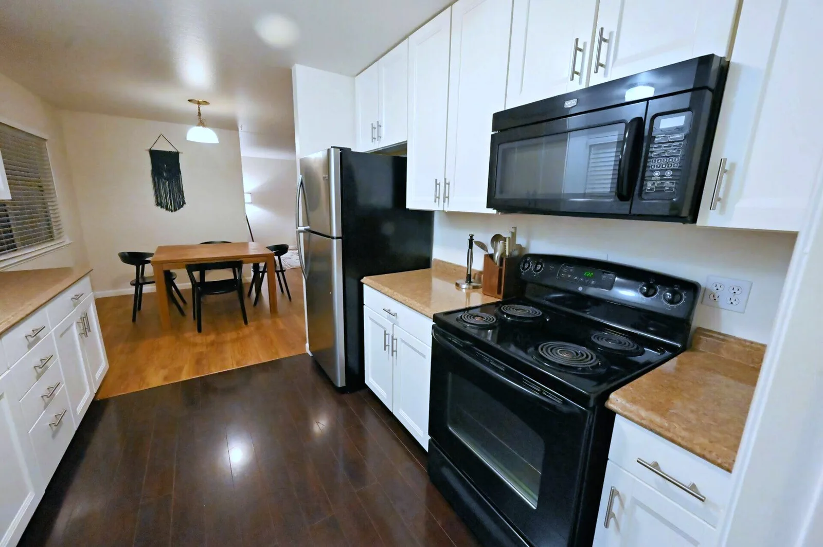Galley kitchen in a Cupertino rental property with white cabinets, a stainless steel refrigerator, and dark hardwood floors.