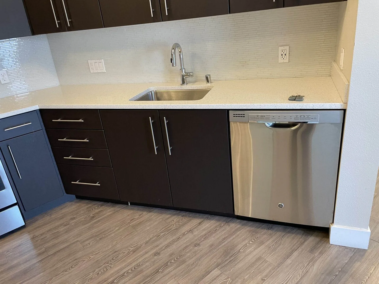 Dark cabinet kitchen with stainless sink, faucet, and an open stainless dishwasher.