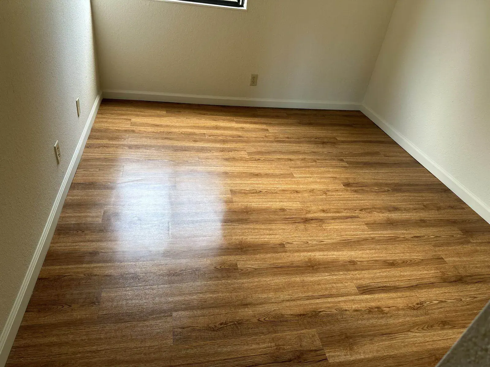 Empty room with glossy laminate flooring and sunlight reflection