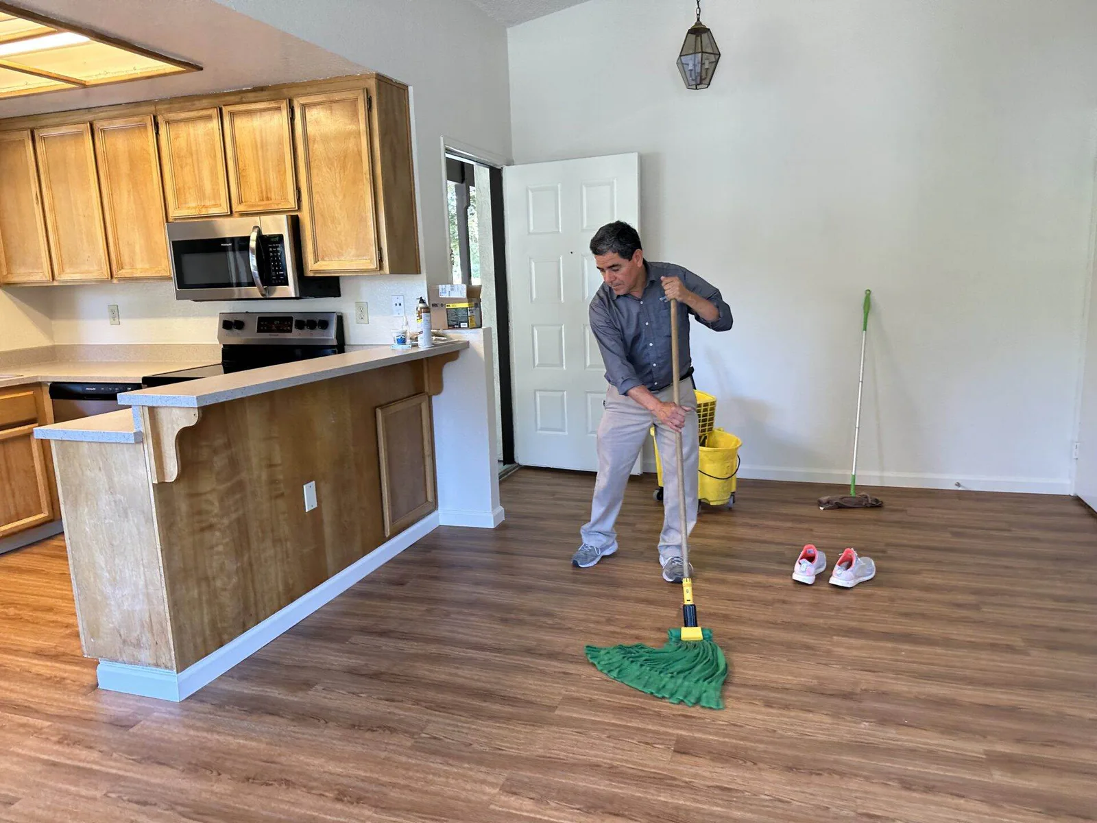 Cleaning technician mopping a laminate floor in an open living room and kitchen