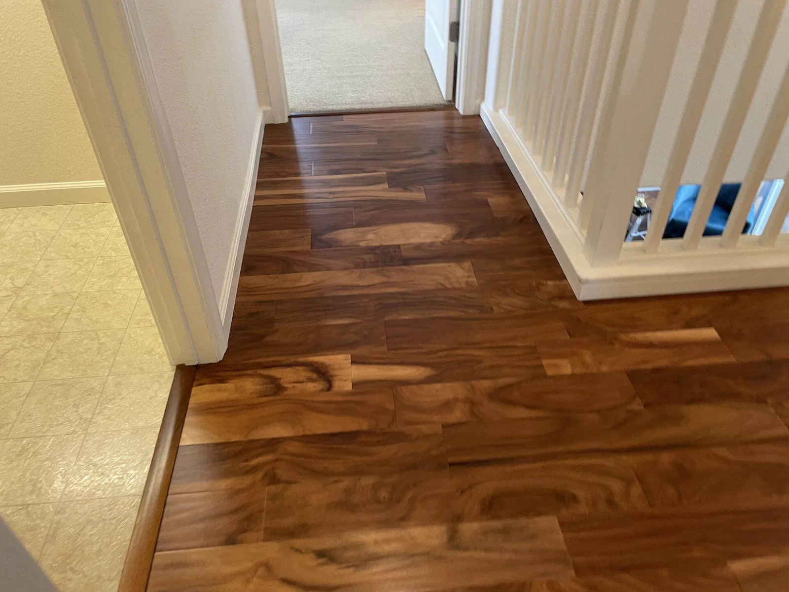 Hallway floor transition from dark hardwood to patterned tile, next to a white stair railing.