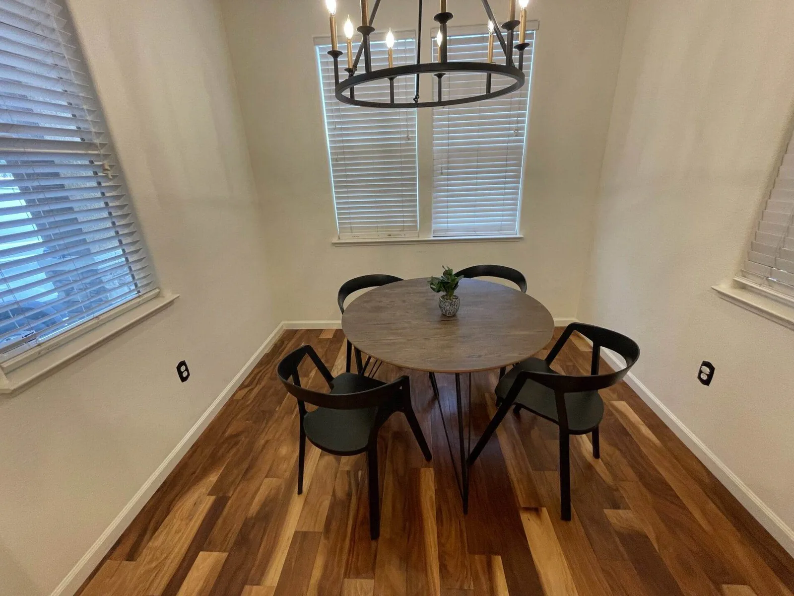 Round wood dining table with black chairs under a chandelier in a San Jose home