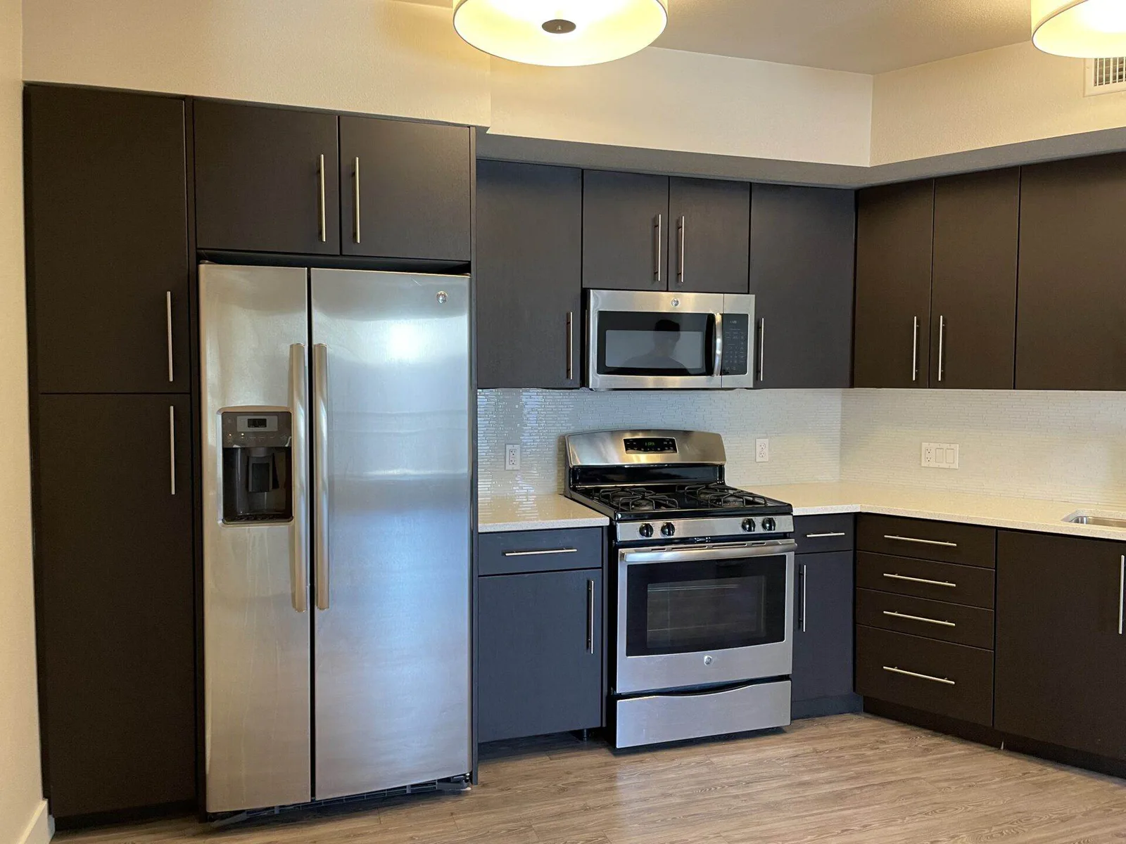 Kitchen with dark cabinetry, stainless steel refrigerator and gas range, and round pendant ceiling lights.