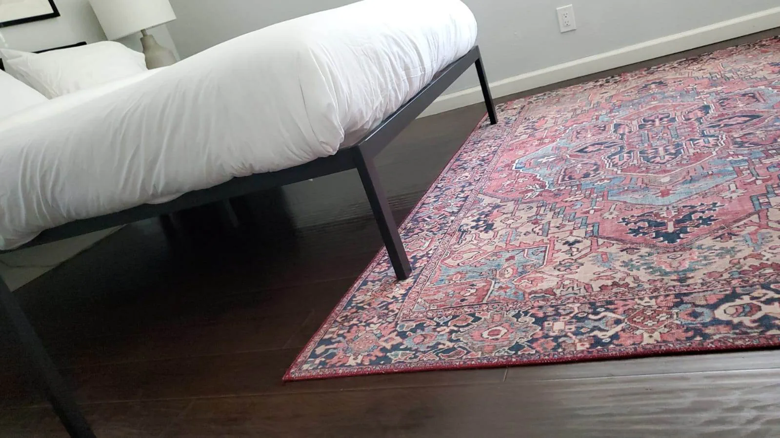 Colorful medallion-pattern area rug next to a bed frame on hardwood flooring after professional cleaning.