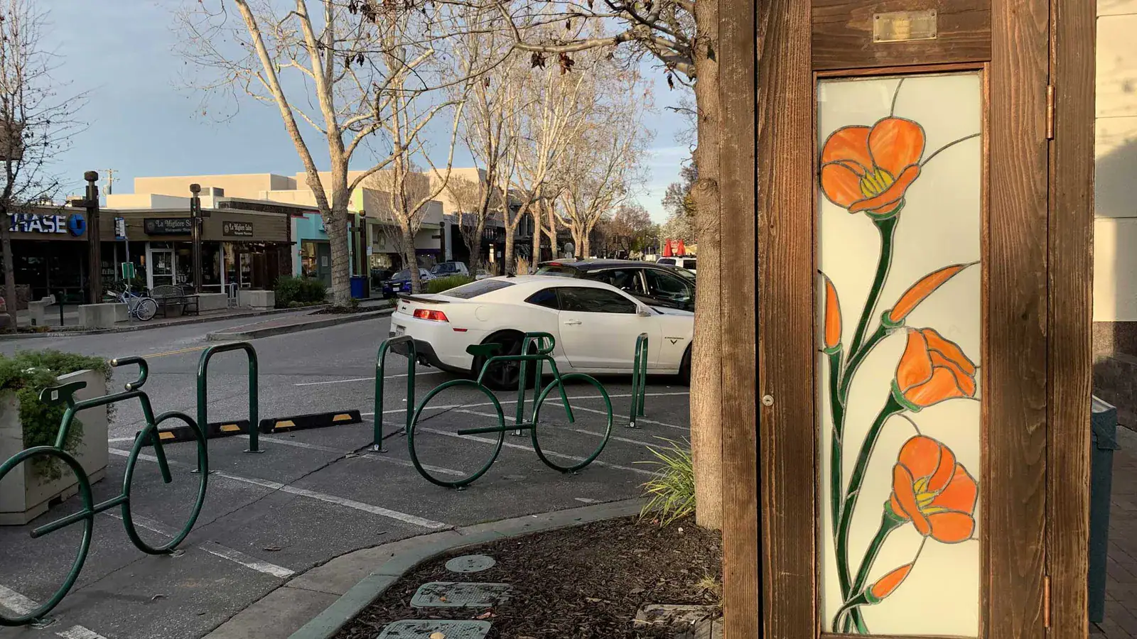 Downtown Menlo Park, California street with storefronts, bike racks, and parked cars lit by late afternoon sun.