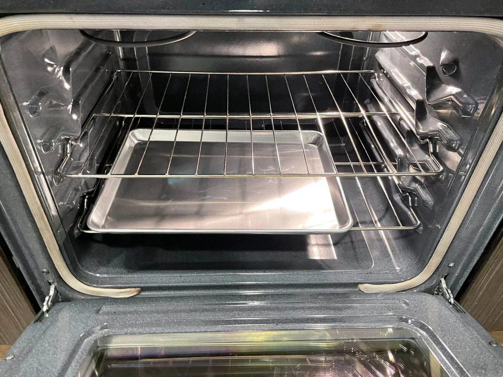 Clean oven interior with a stainless steel baking sheet resting on the middle rack.