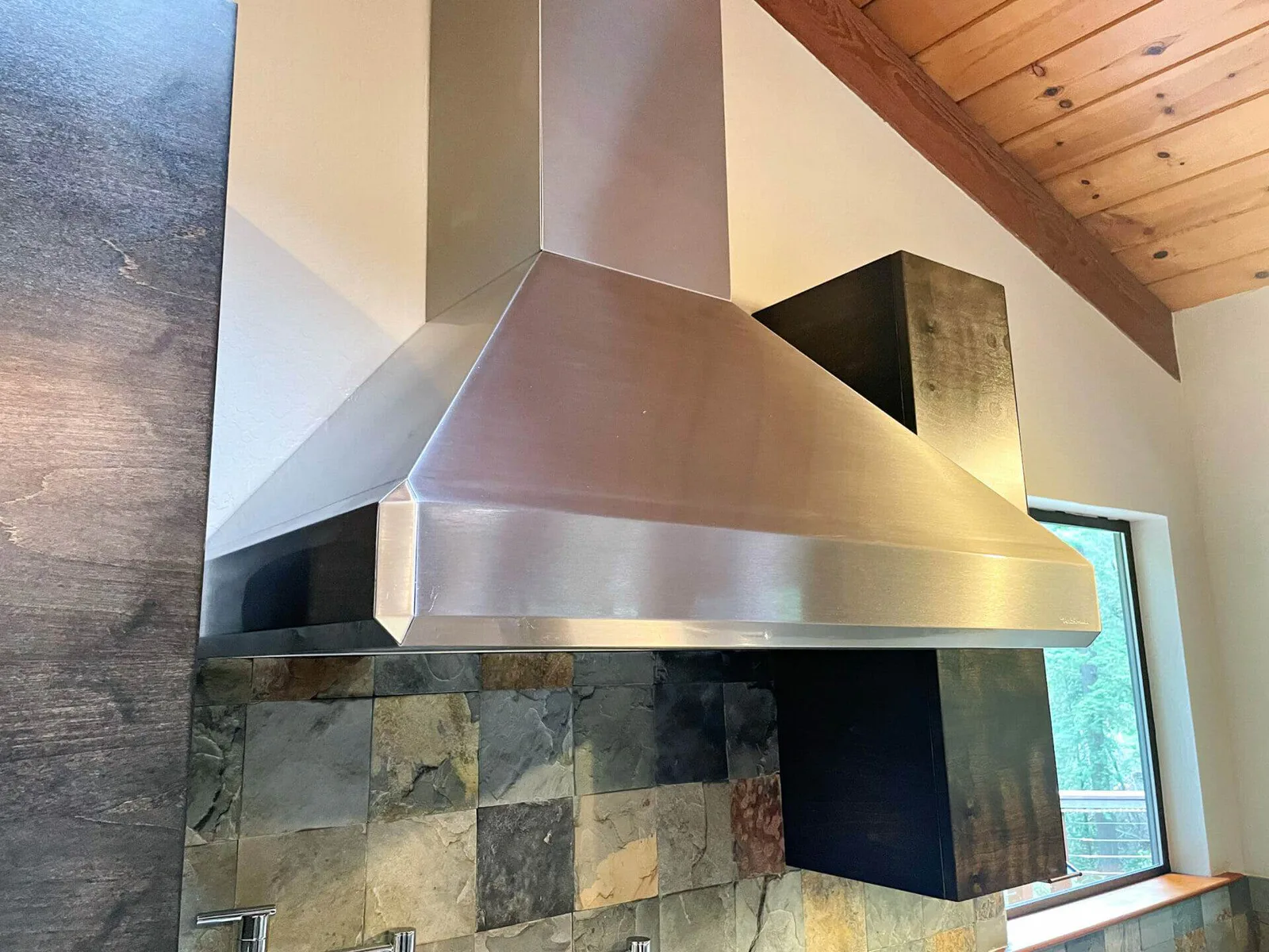 Stainless steel range hood and slate tile backsplash after kitchen hood cleaning.