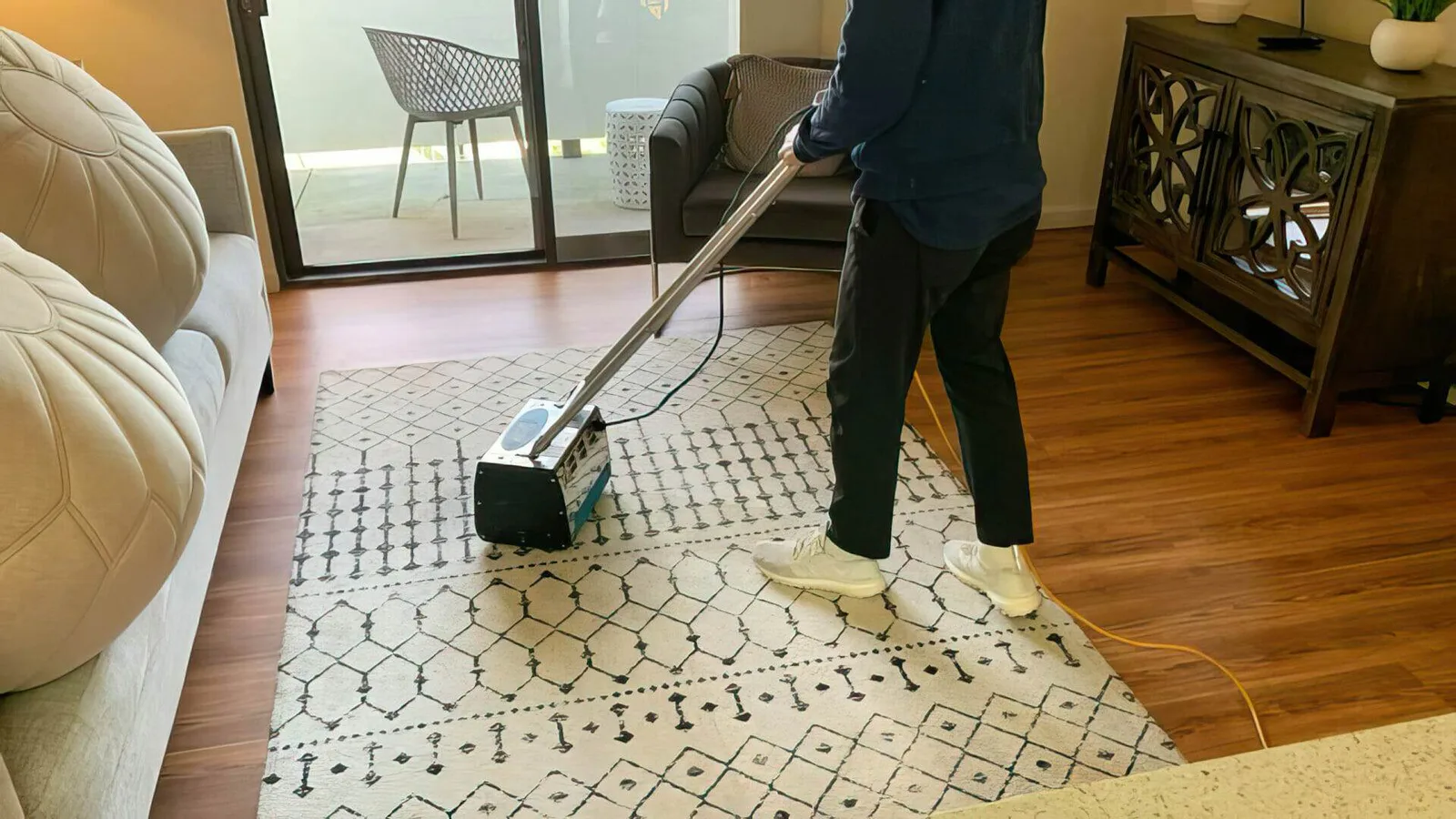 Technician deep cleaning a patterned area rug in a living room with a rug cleaning machine.