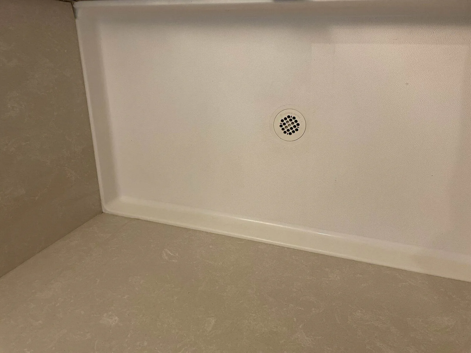 Close-up of a clean white textured shower pan floor with a round drain.