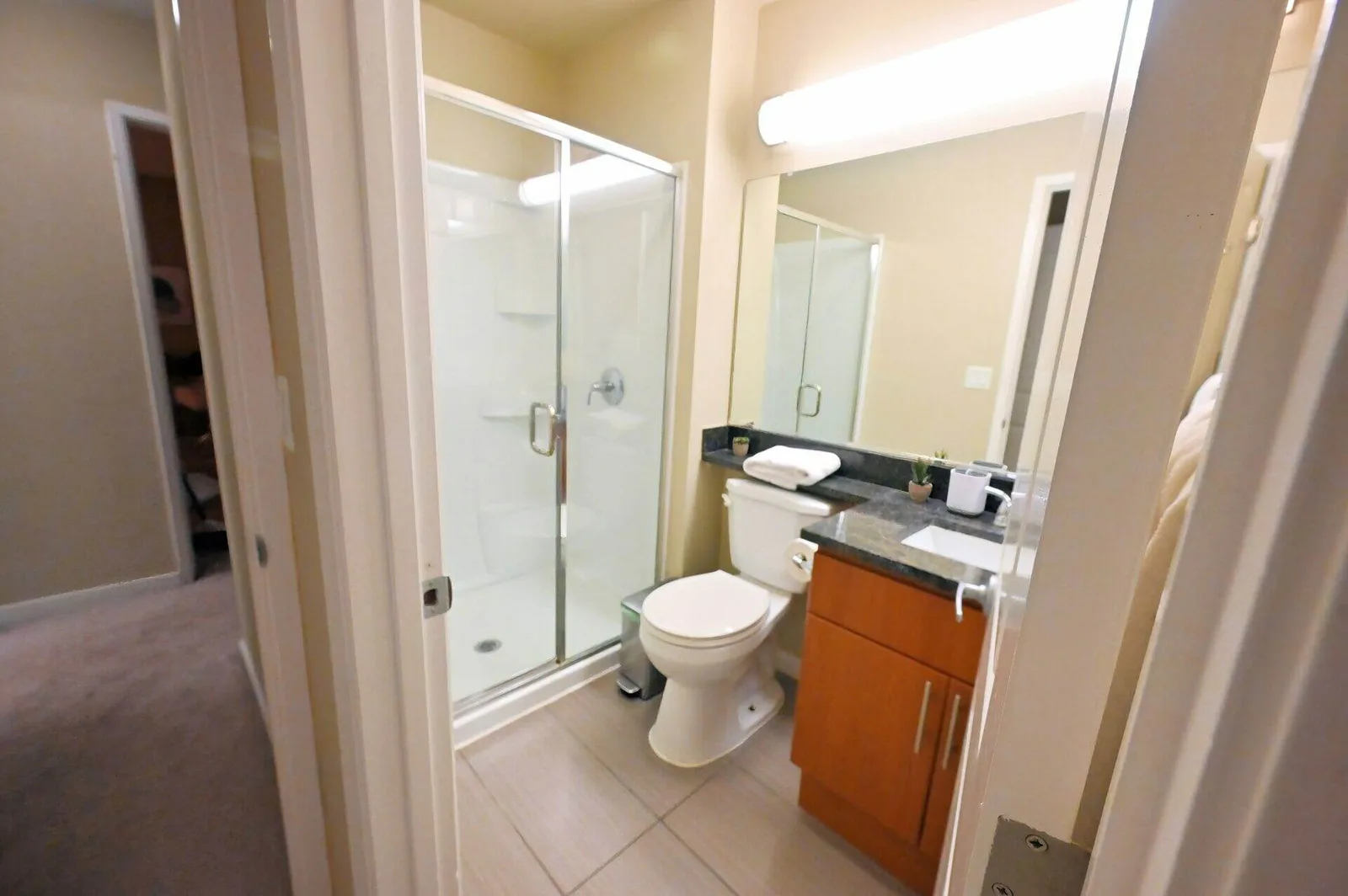 View from the hallway into a tidy Sunnyvale apartment bathroom with glass shower door and wood vanity.