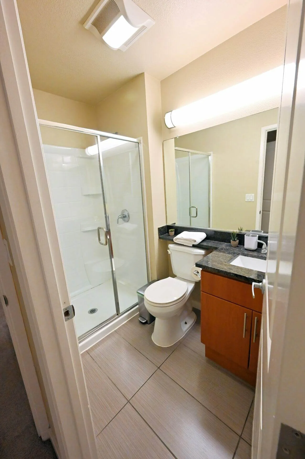 Clean bathroom in a Sunnyvale apartment with a glass shower stall, toilet, and dark stone vanity countertop.