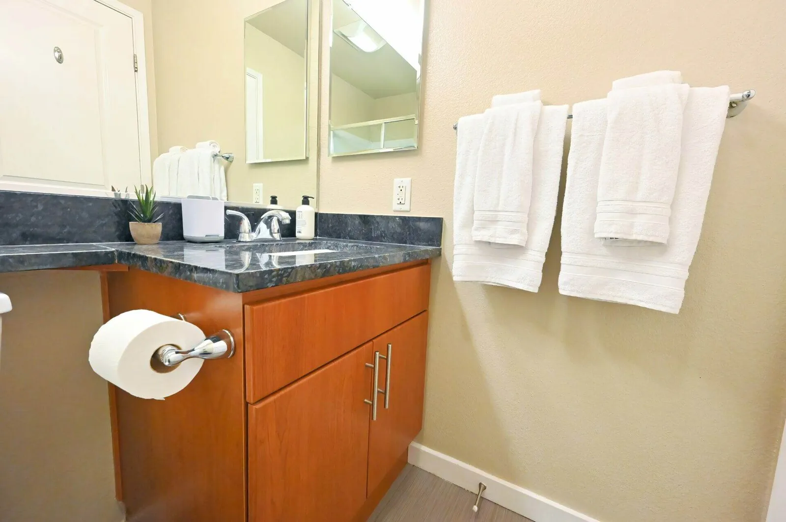 Bathroom vanity close-up with granite countertop, mirror, and folded white towels hanging on the wall.