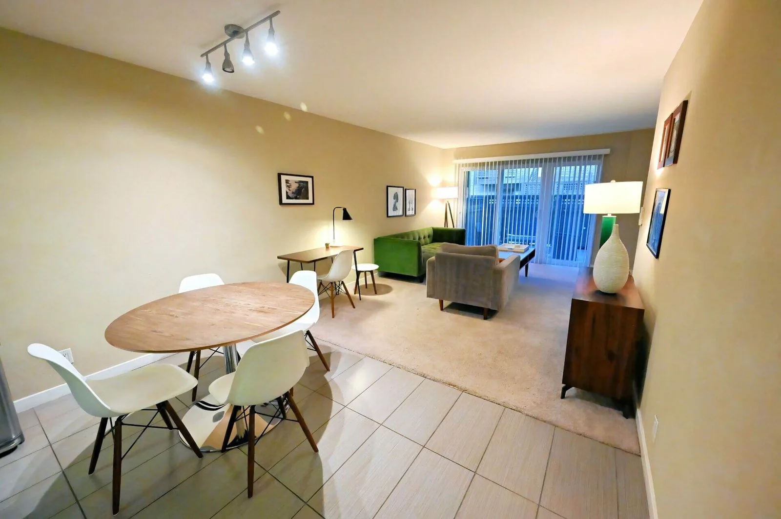 Open-plan dining and living room with a round wood table, white chairs, and a green tufted sofa.