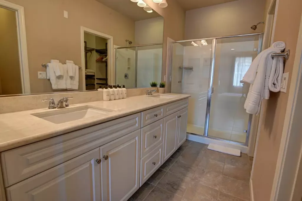 Bathroom with a long double vanity, toiletry bottles lined up on the counter, and a glass shower enclosure.
