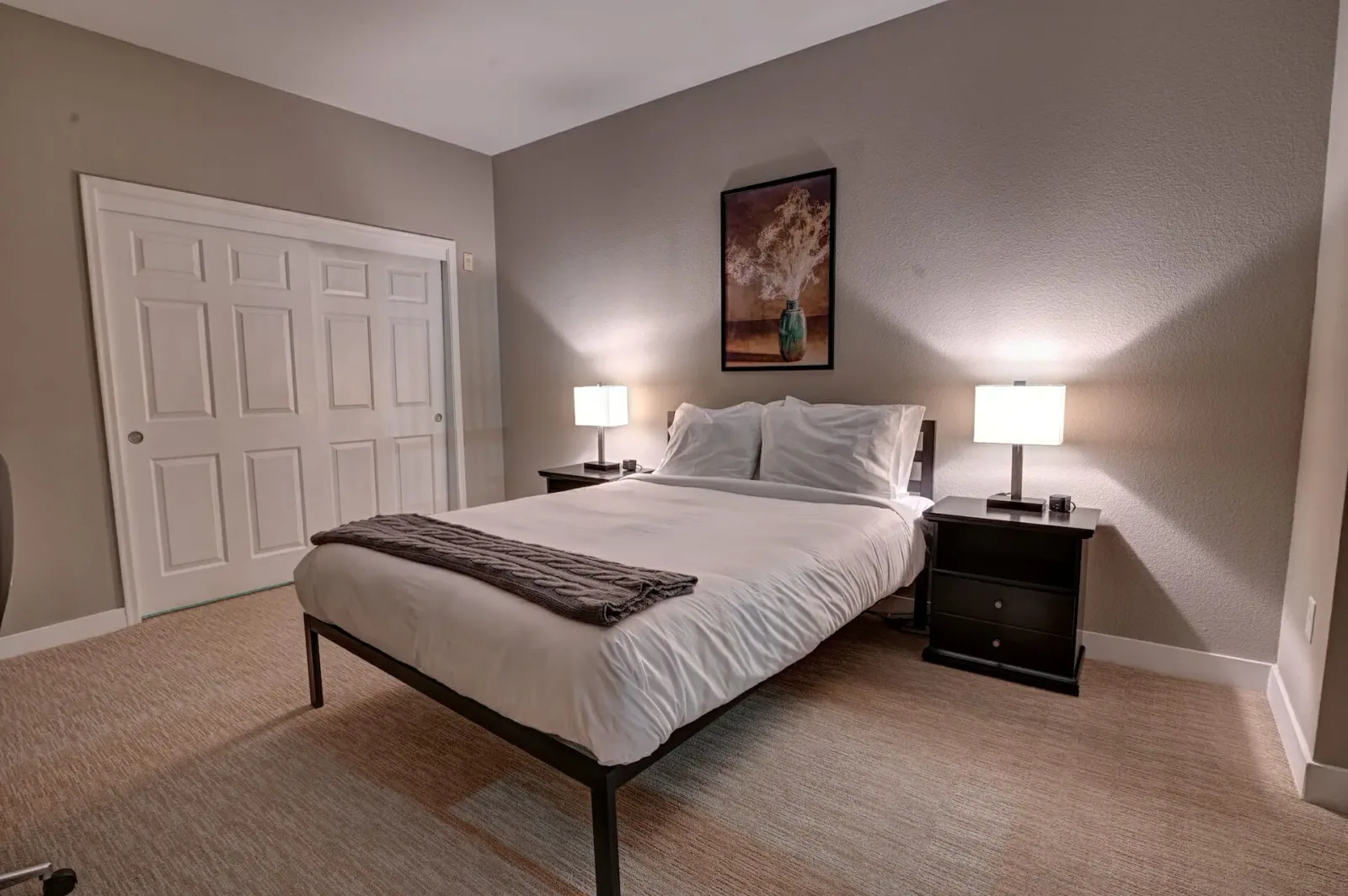 Bedroom with a black metal bed frame, white bedding, gray throw blanket, and a white paneled closet door.
