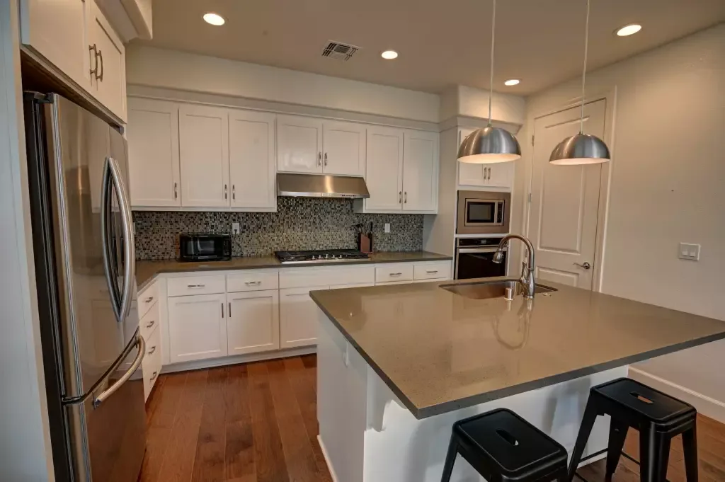 Kitchen with a stainless refrigerator, gas cooktop, and white island under two pendant lights.