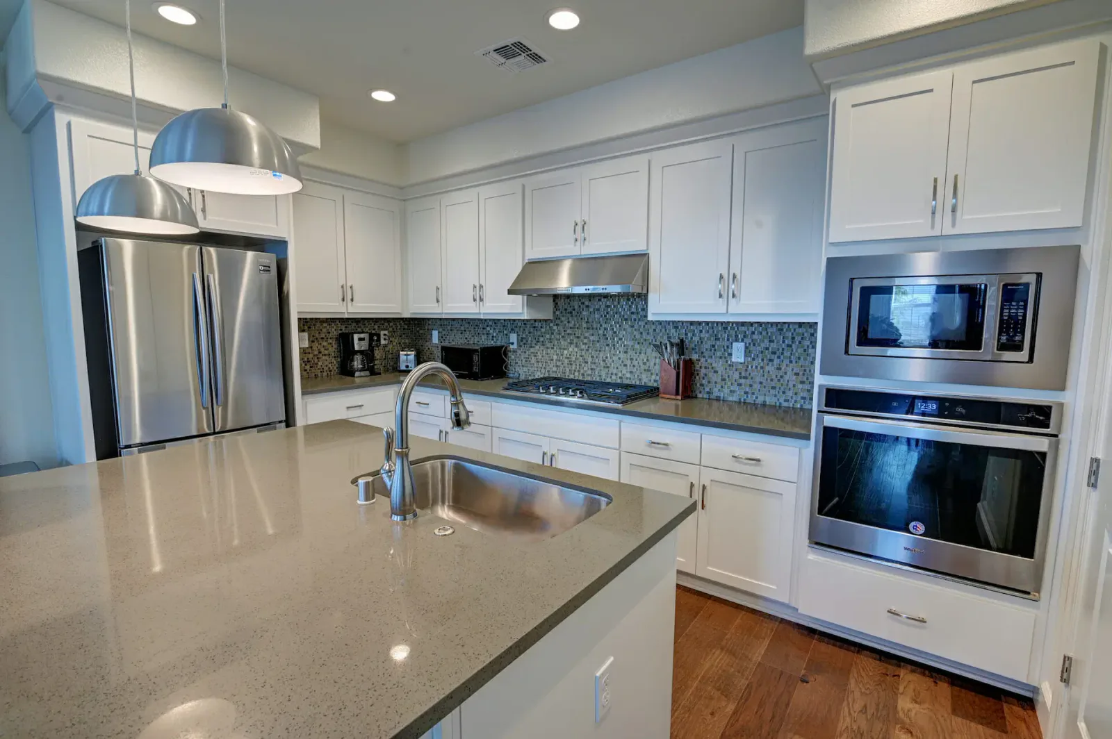 Close view of a kitchen island with a stainless steel sink, gooseneck faucet, and pendant lights overhead.
