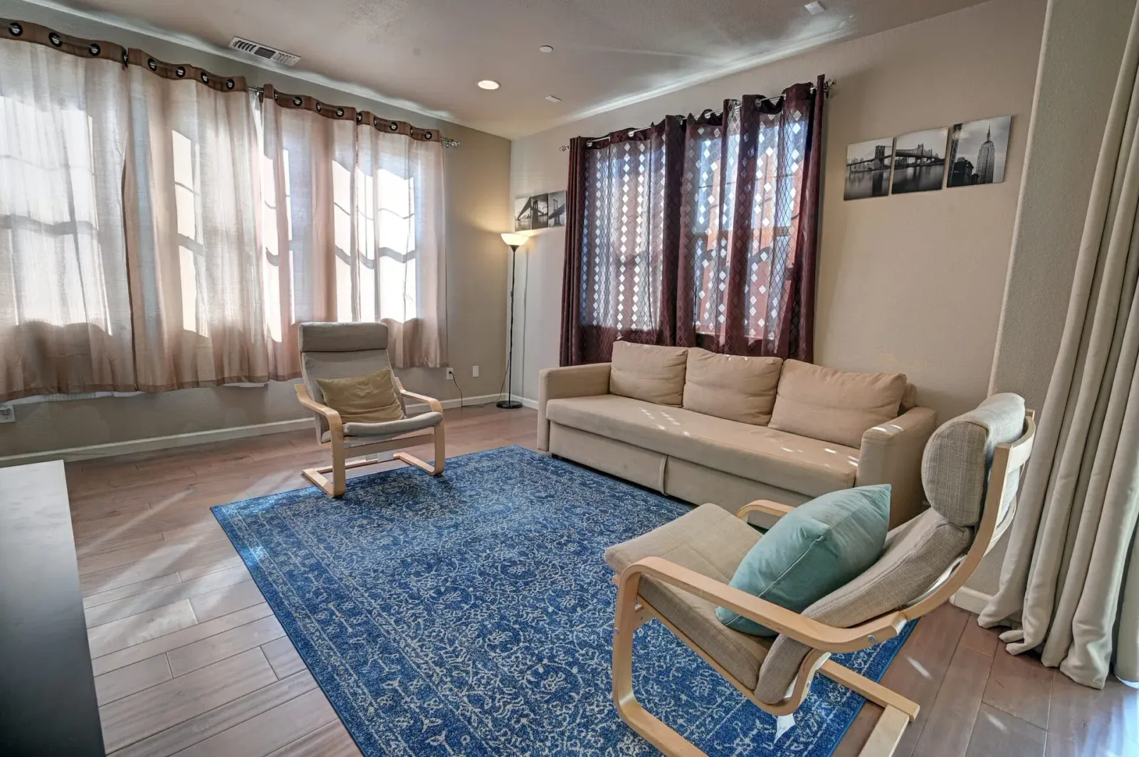 Living room with a beige sofa, wood-frame accent chairs, and framed black-and-white New York City photos on the wall.