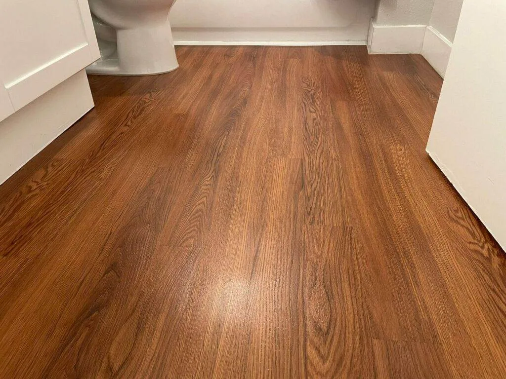 A bathroom with wood floors and a toilet that requires cleaning.