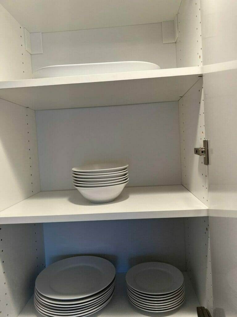 A white cupboard with plates and bowls, serving as kitchen cabinetry.