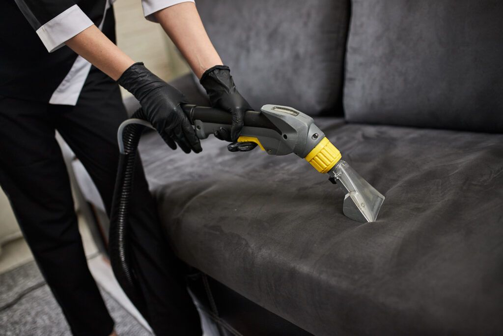 A woman in San Jose using a vacuum cleaner to clean a couch in her living space.