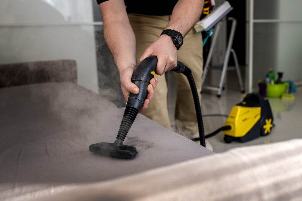 A man in San Jose expertly cleaning a couch with a steam cleaner in his living space.