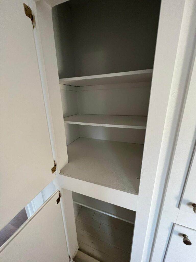 An empty white cabinet with open doors and three empty shelves.
