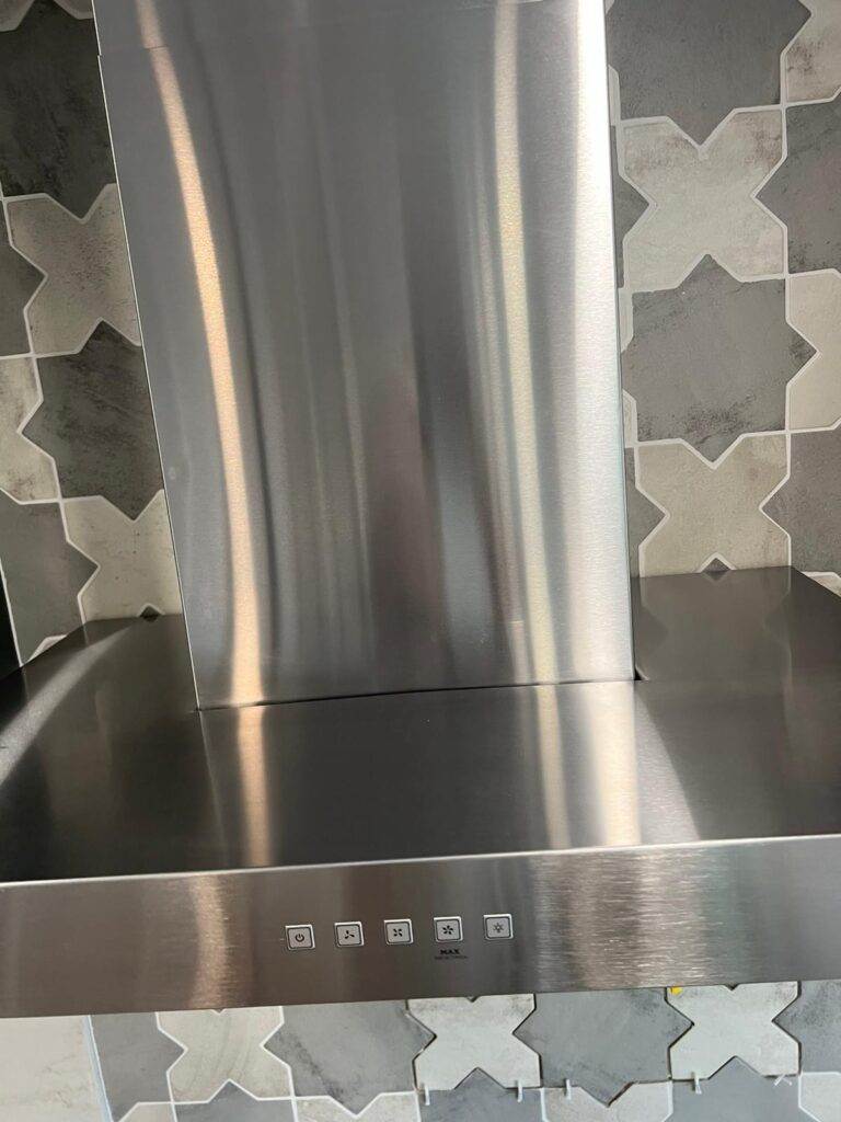 Stainless steel kitchen backsplash with control buttons and patterned wall tiles.