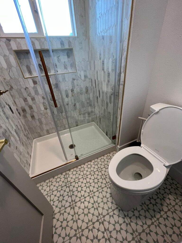 A contemporary bathroom with a geometric tile floor, a corner shower stall with a glass door, and a white toilet.