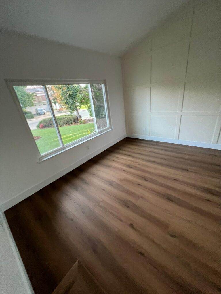 Empty room with wooden flooring and a large window overlooking a lawn.