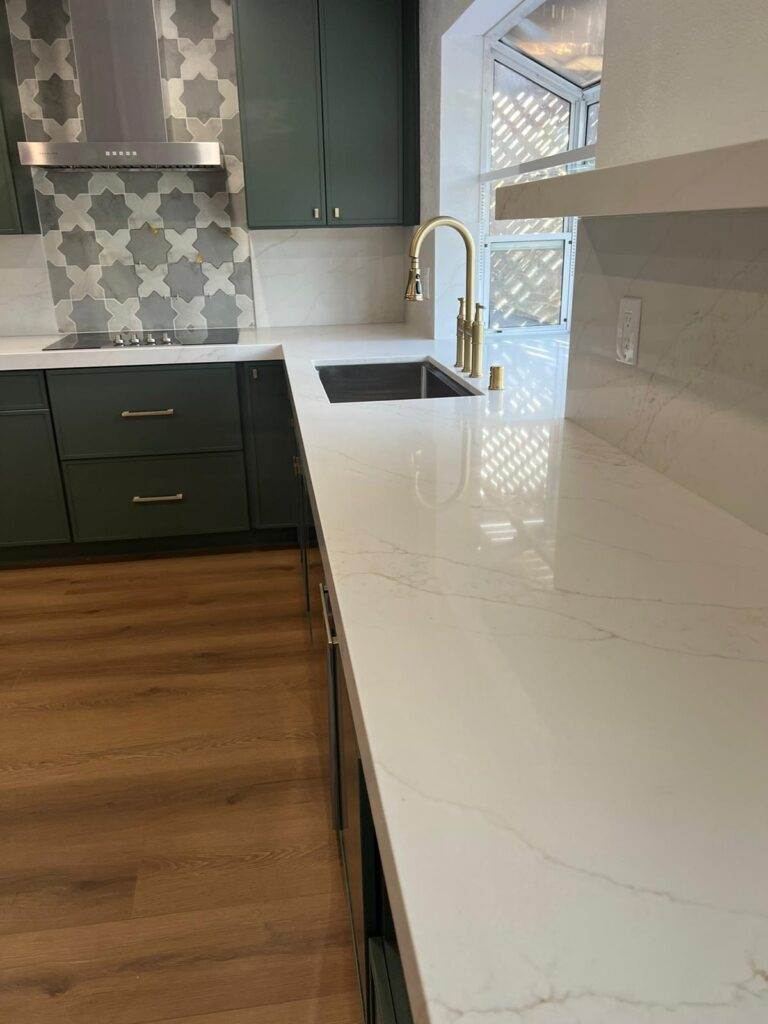 Modern kitchen with white marble countertops, dark green cabinets, and a gold faucet.