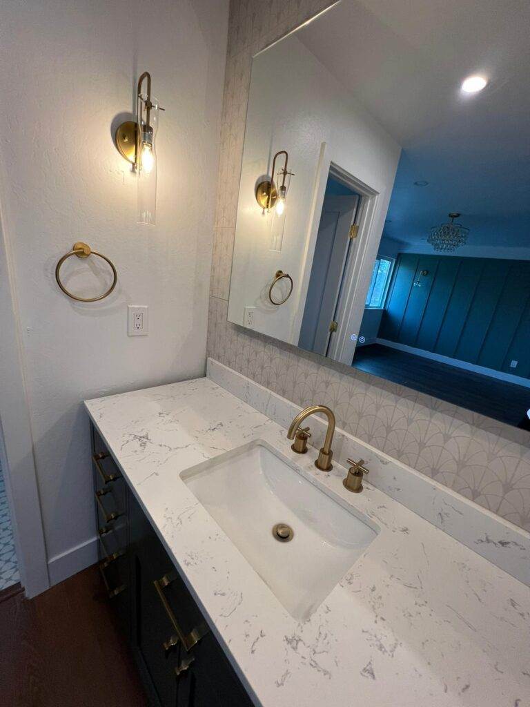 Modern bathroom interior with a wall-mounted sink, brass fixtures, and decorative mirror.