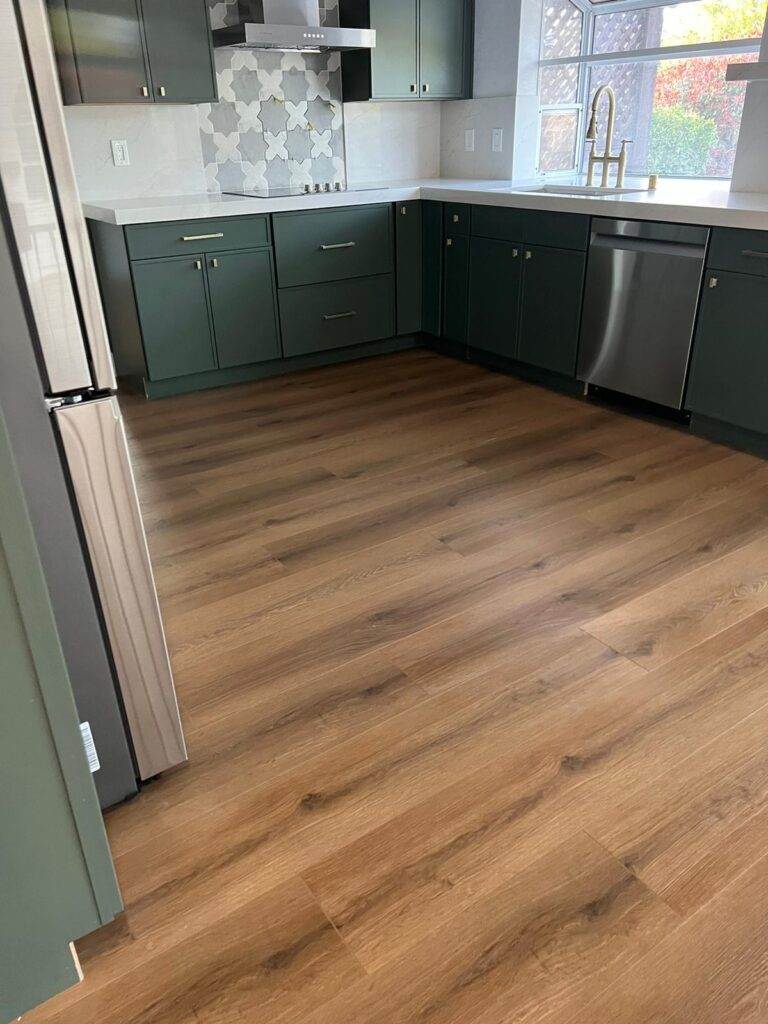 A modern kitchen with green cabinets, stainless steel appliances, and wood-style flooring.