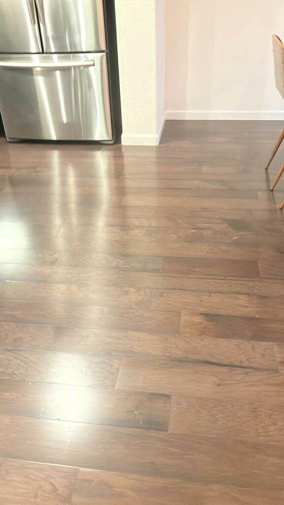 A modern kitchen with shiny wooden flooring, serviced by Master Clean Service, featuring a stainless steel refrigerator and a wooden chair partially visible.