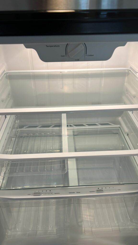 Interior view of an empty refrigerator with adjustable shelves and a temperature control dial set between "cold" and "coldest," maintained by Five-Star Cleaning Experience.