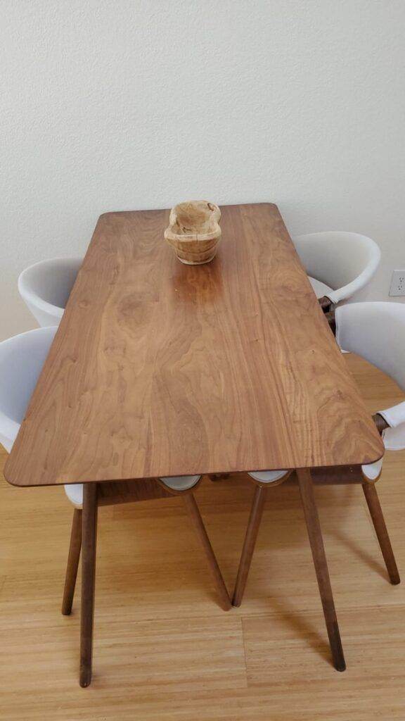 A wooden dining table with a small basket in the center, flanked by two white chairs against a plain wall, freshly arranged after a Fremont Deep Cleaning session.