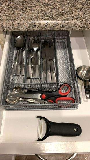 A kitchen drawer organizer filled with assorted utensils including spoons, forks, a measuring cup, scissors, and a peeler is meticulously cleaned by Master Clean Service.