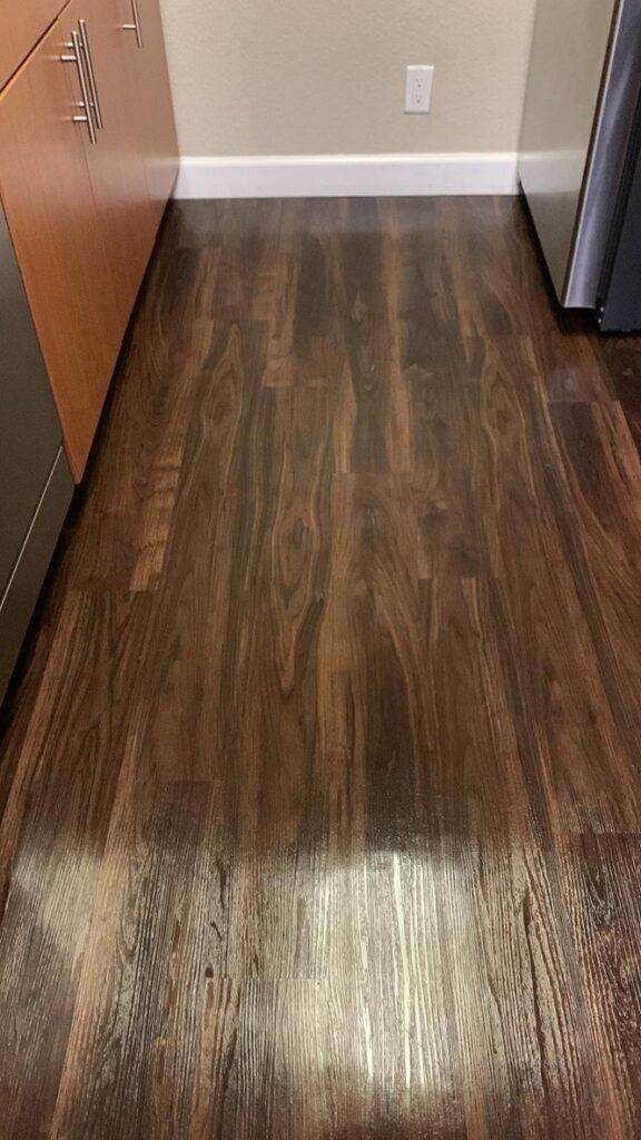 Dark wood laminate flooring in a room corner with cabinets and an electric outlet visible, recently updated by Union City Post Construction Cleaning.