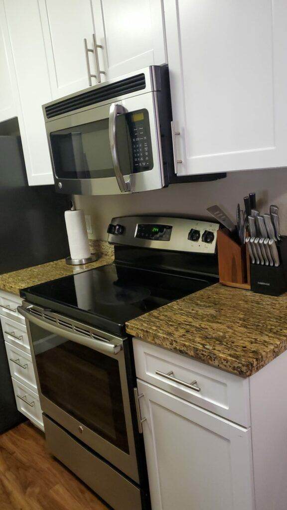 A modern kitchen with stainless steel appliances, granite countertops, white cabinetry, and a set of knives, perfectly maintained by Master Clean Service.