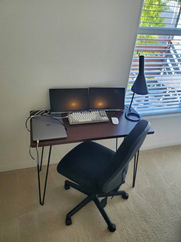 A professional home office setup in Union City with a desk, two monitors, a laptop, a mechanical keyboard, and an ergonomic chair near a window with blinds.