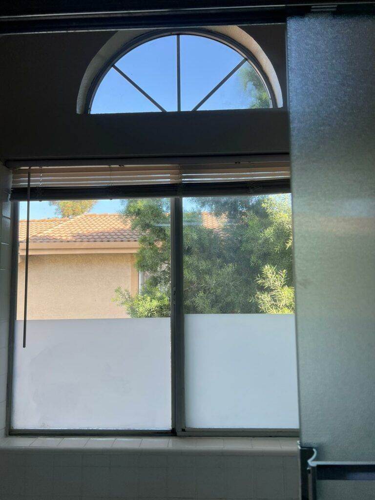 A window with a semi-circular arch at the top, displaying a view of a residential area and trees under a clear blue sky, freshly cleaned by Santa Clara Post Construction Cleaning.