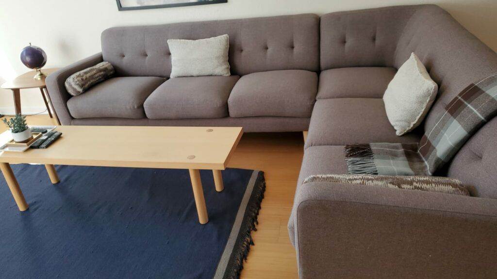 A modern living room featuring a large gray upholstered sectional sofa with cushions, a wooden coffee table, and a blue rug.