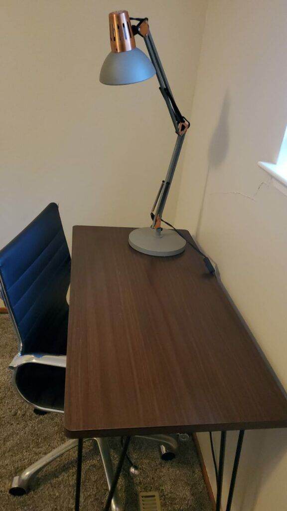 A small wooden desk with a metal chair and an adjustable metallic lamp in a room, maintained by Master Clean Service.